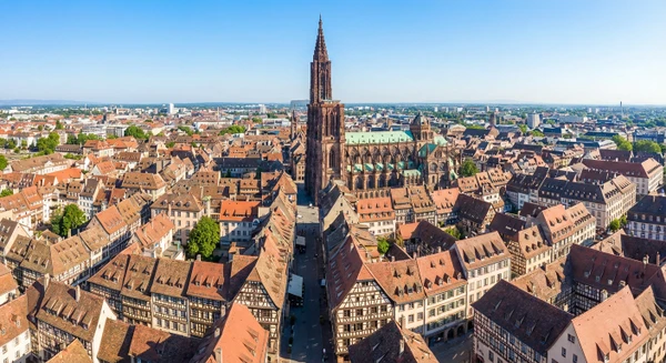Photographie professionnelle aérienne ou perspective élevée de Strasbourg montrant la cathédrale et le centre historique avec l'architecture alsacienne typique (maisons à colombages, toitures de tuiles), entouré par le tissu urbain et les paysages environnants. L'image doit être prise par beau temps avec un ciel dégagé, offrant une vue claire et accueillante qui illustre cette ville majeure de la zone d'intervention du chauffagiste ADAO (rayon de 40 km autour de Colmar).