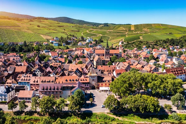 Photographie professionnelle du village de Turckheim en Alsace, montrant une vue du centre-bourg avec l'architecture alsacienne typique (maisons à colombages, toitures de tuiles colorées), captée par beau temps avec un ciel dégagé. La perspective doit être suffisamment large pour montrer l'environnement villageois et les paysages alentour (vignobles, collines), évoquant clairement la zone géographique de Turckheim dans le Haut-Rhin où intervient le chauffagiste ADAO.